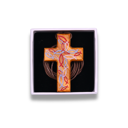 Handcrafted olive wood cross necklace featuring intricate red and light blue Ichthus fish engravings forming a woven pattern on the surface, suspended on a brown cord. In a gift box.