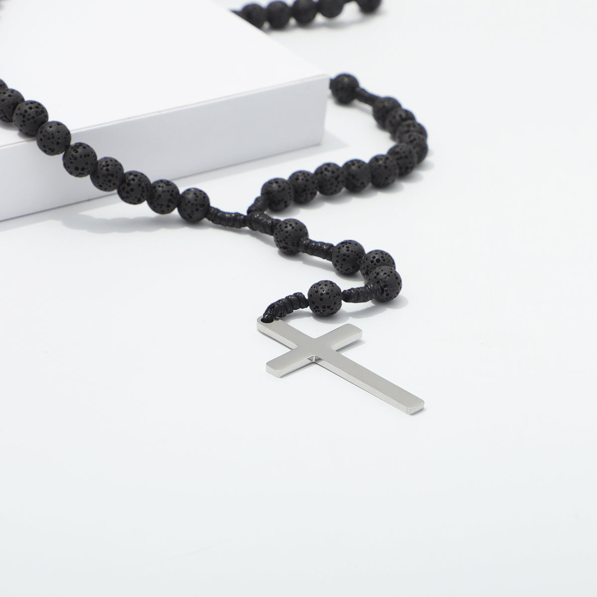 Close view of the plain metal cross and lava beads on knotted cord