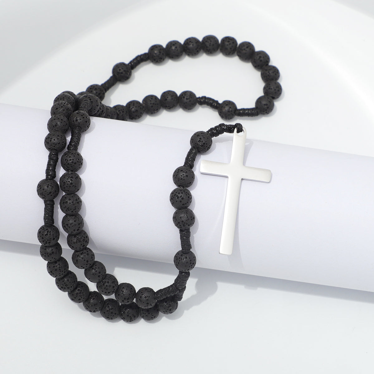Lava stone prayer rosary and plain metal cross draped over white blocks