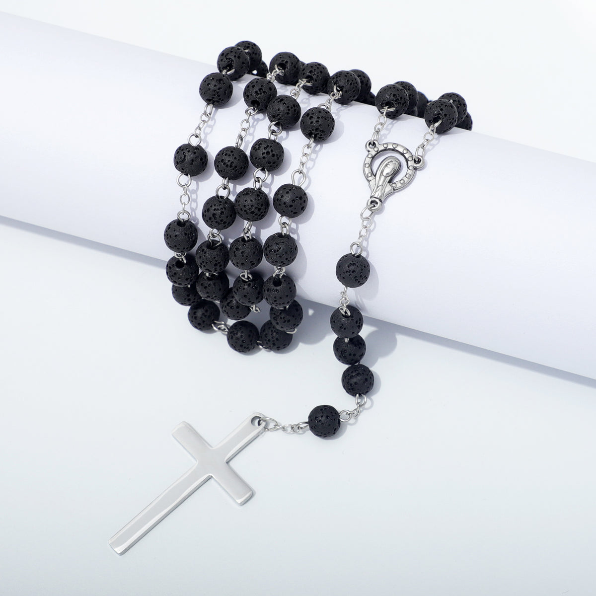 Lava stone rosary and metal cross draped over a white block