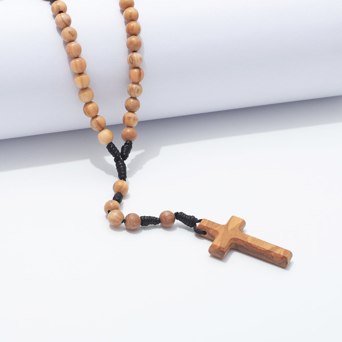 A wooden bead rosary necklace with a wooden cross pendant, featuring light brown olive wood beads, a black cord section, and a carved wooden cross, displayed on a clean white background.