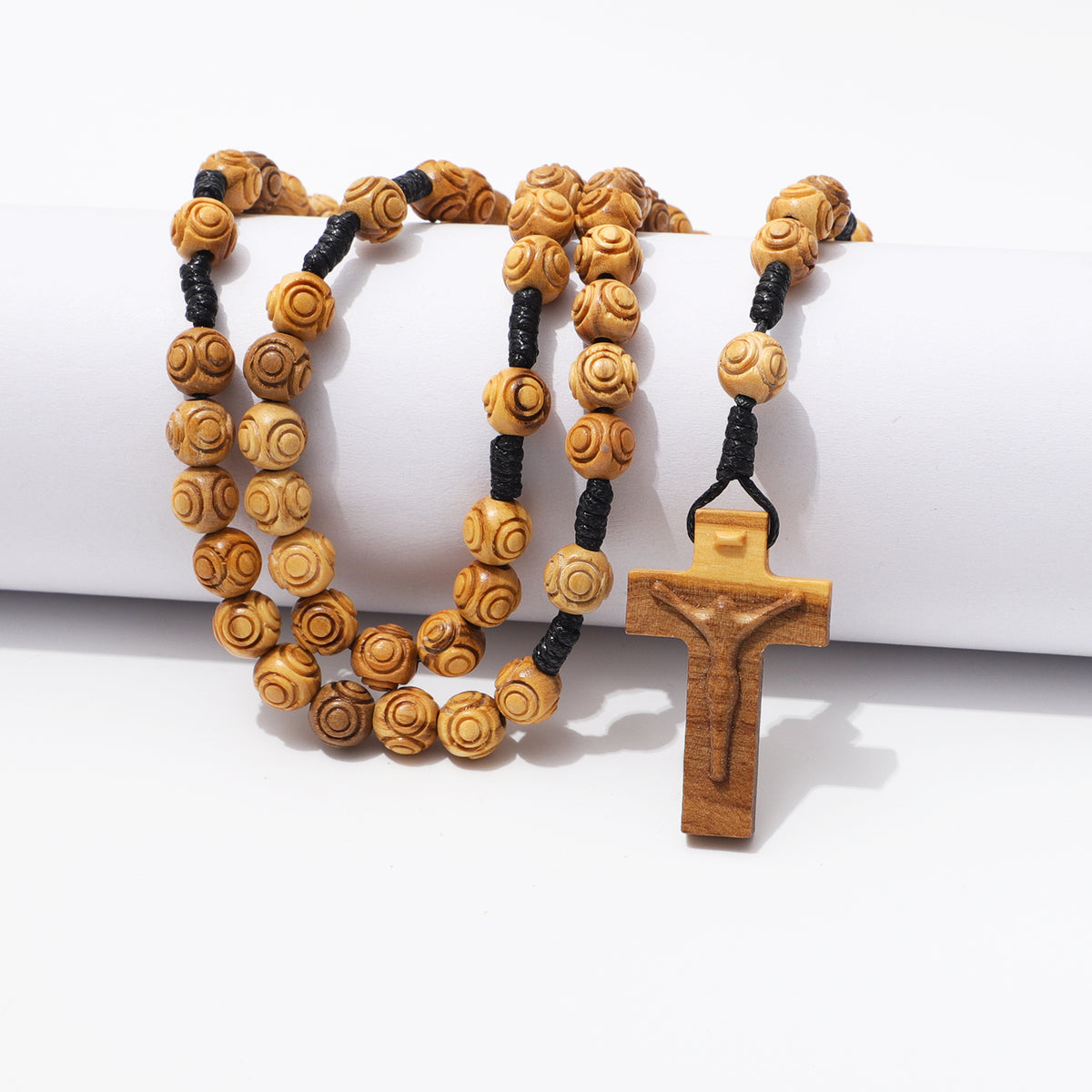 Engraved olive wood beads and carved crucifix draped over a white block