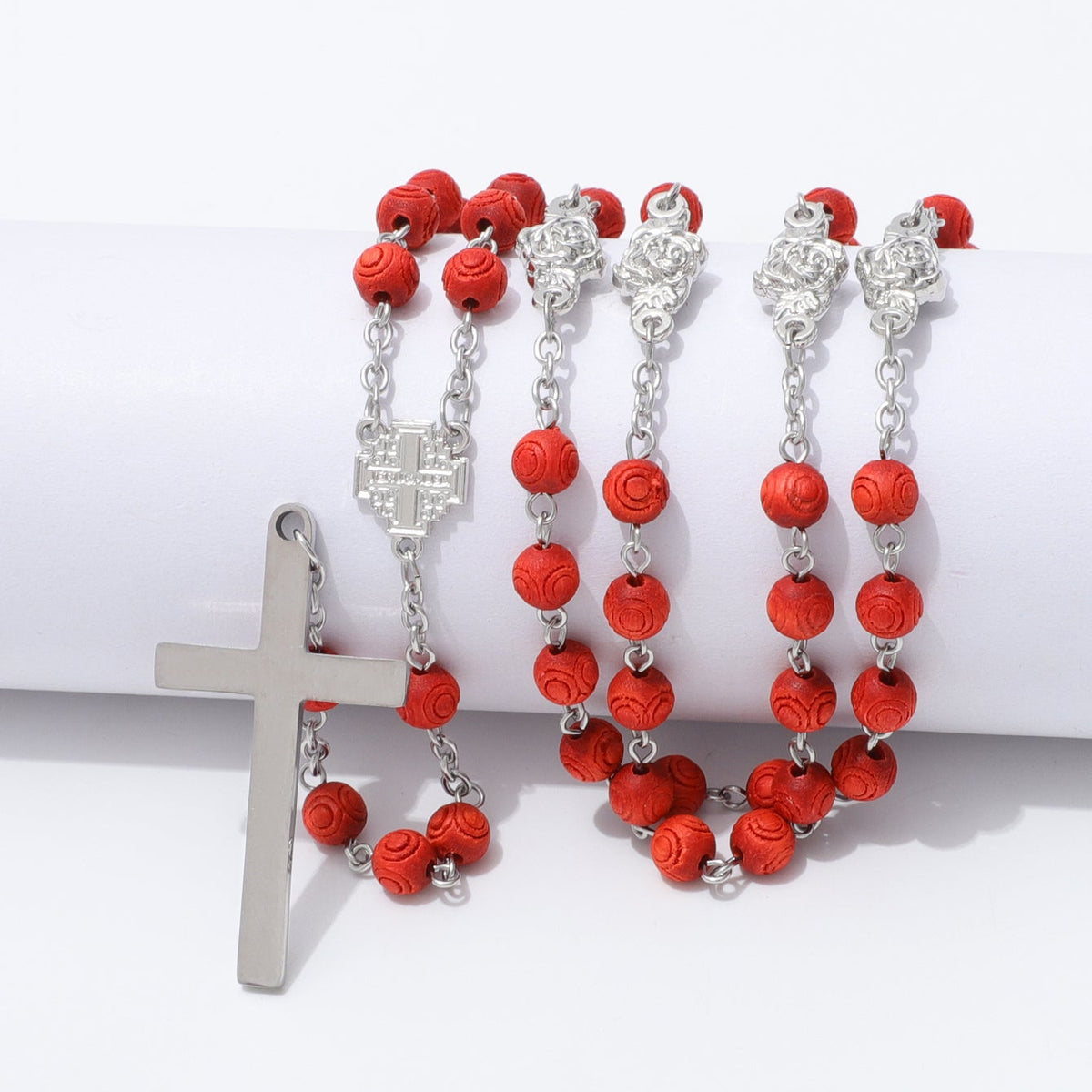 Engraved red wooden rosary beads and polished cross draped over a white block