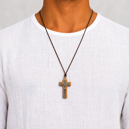 A wooden crucifix pendant with a silver-toned metal corpus and a brown cord loop at the top, shown on a model