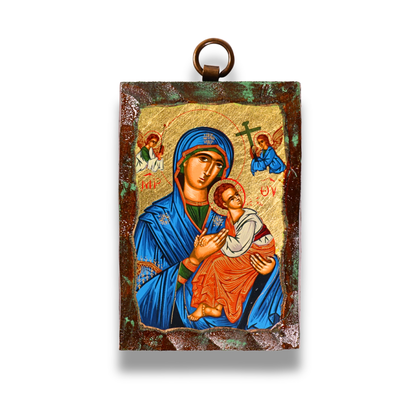 An icon of the Virgin Mary in a blue robe holding the child Jesus, with both figures haloed against a gold leaf background. Above them are two angels, and the icon is bordered by a dark, textured frame with a metal loop at the top for hanging.