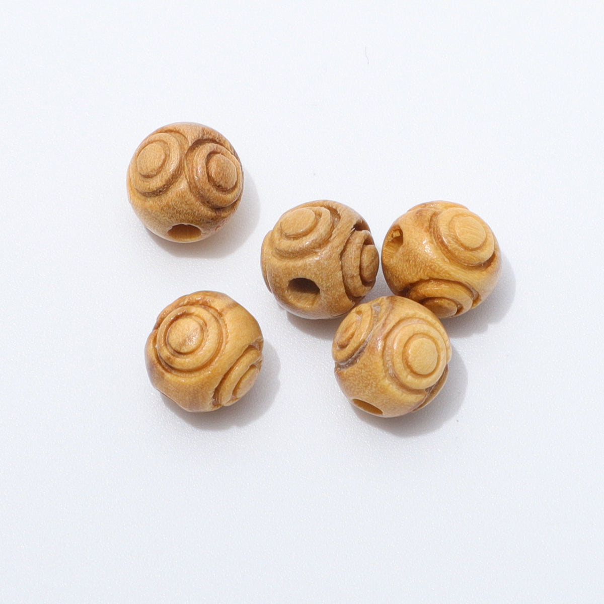 Close up of five loose 8mm engraved olive wood beads showing circular patterns