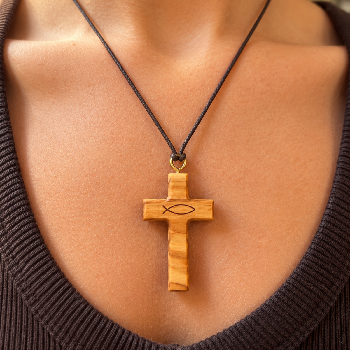 A close-up of a person's chest wearing a wooden cross pendant necklace on a dark cord, with a small fish symbol engraved on the cross.