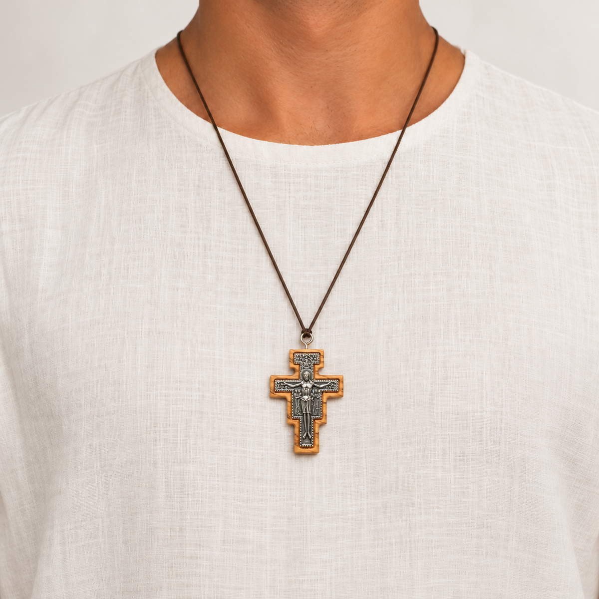 San Damiano olive wood crucifix necklace worn on a brown cord over a white shirt.