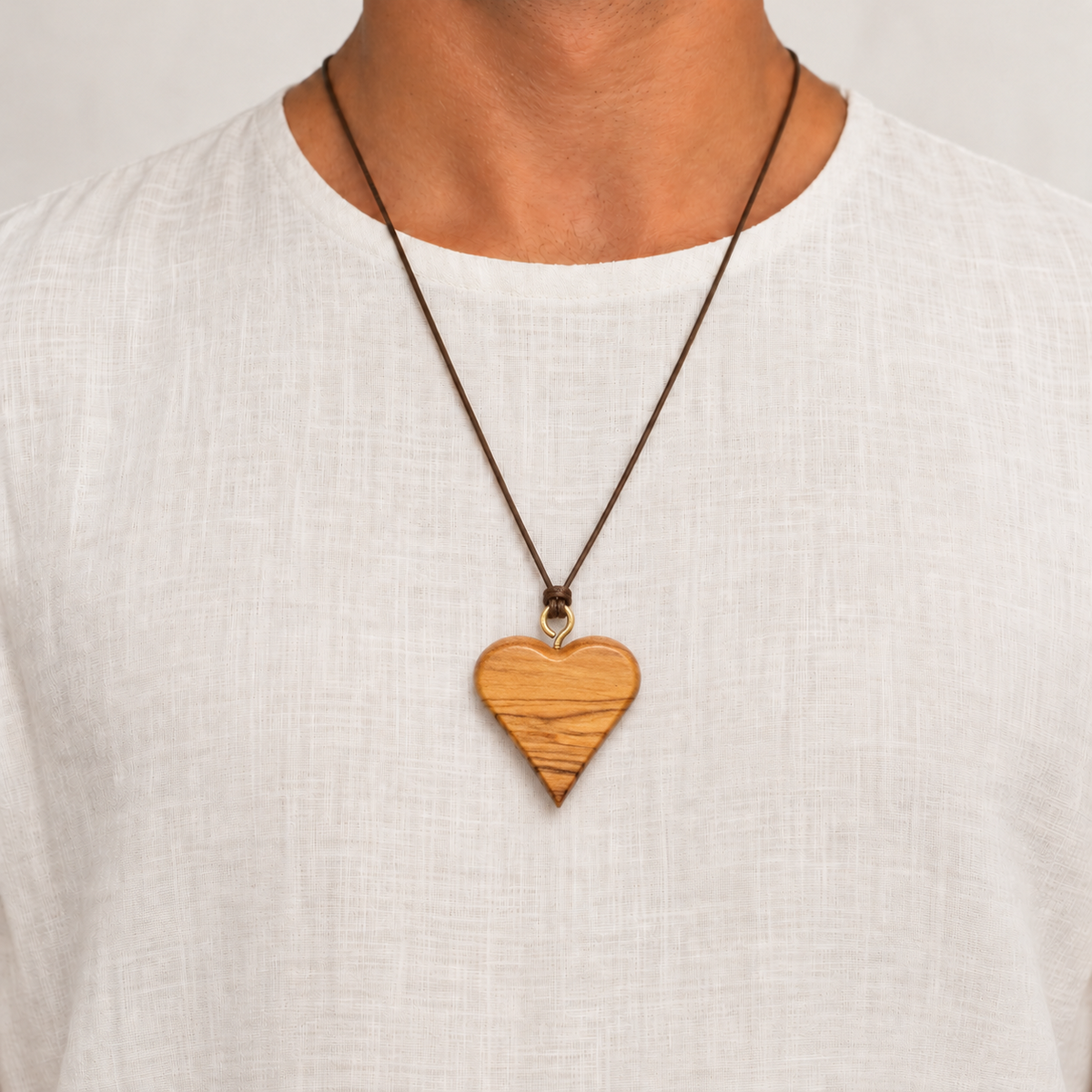 Ahavah olive wood heart necklace worn on a brown cord over a white shirt, showing how the pendant sits on the chest.